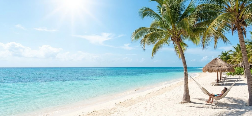 Couple relaxing in a hammock on a Riviera Maya beach with sunny weather, turquoise sea, and white sand free of sargassum.