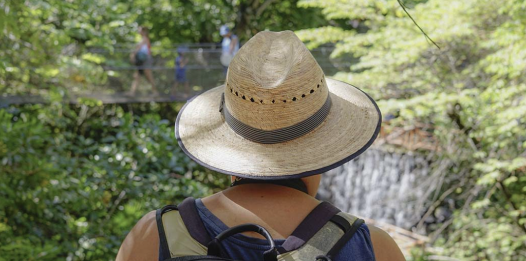 Persona con sombrero de paja y mochila observando un puente colgante en medio de una selva tropical de México.