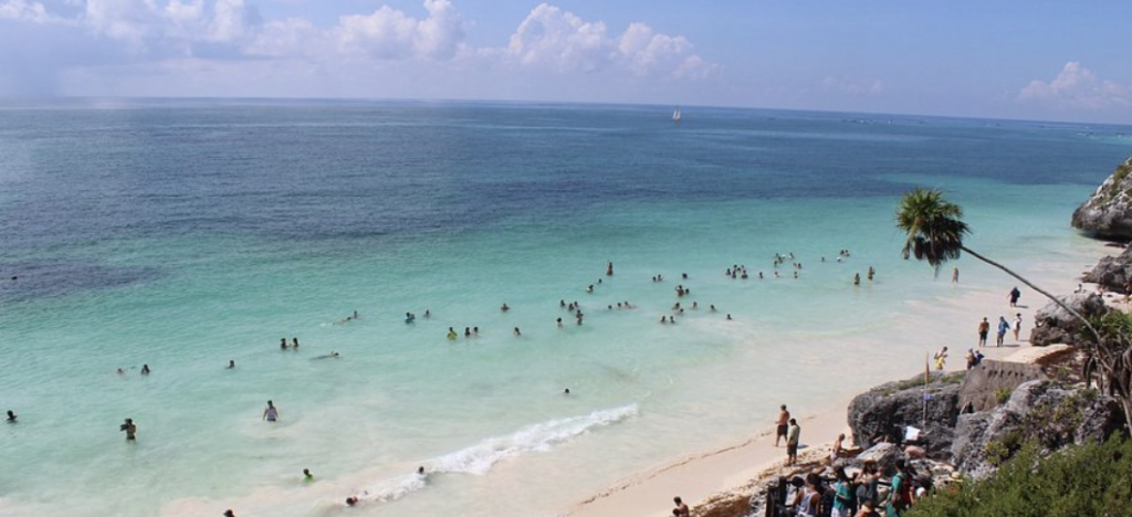 Hotel boutique de lujo con arquitectura de palapa frente al mar Caribe y palmeras.