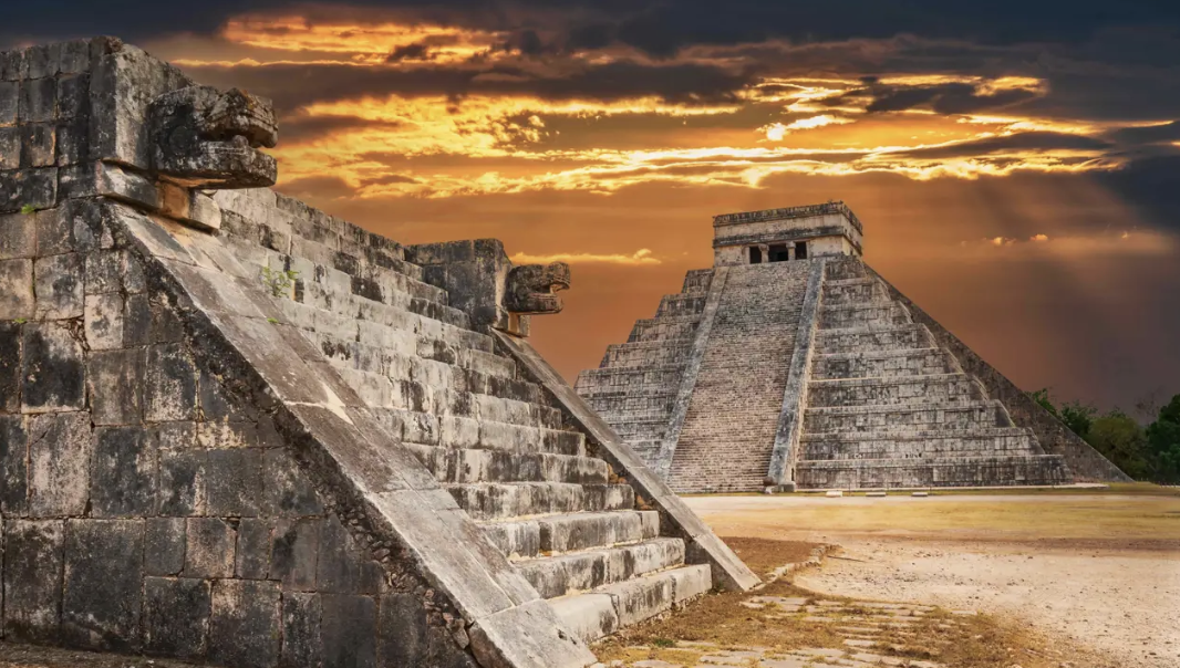 Pirámide de Kukulcán en Chichén Itzá bajo un cielo de atardecer con cabezas de serpiente emplumada en primer plano.