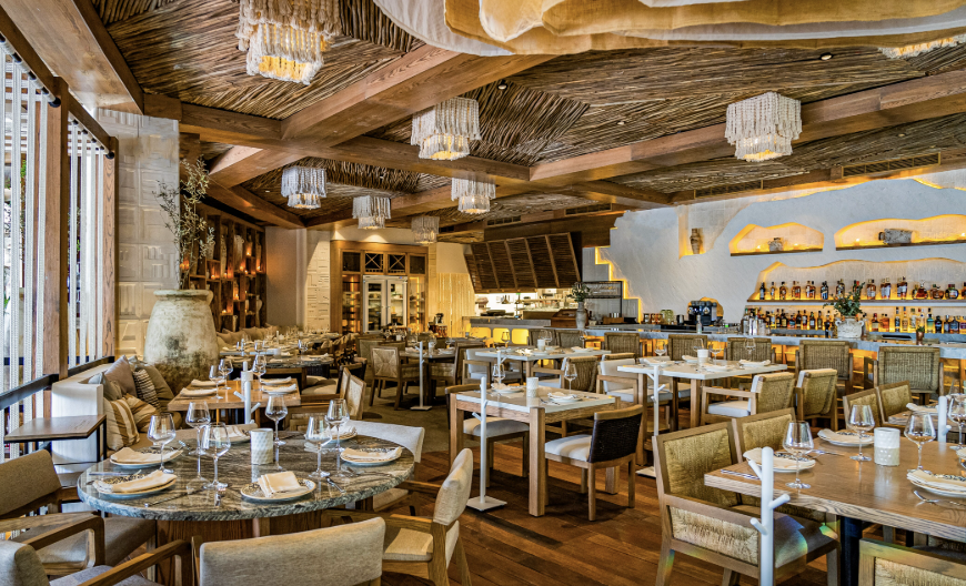 Interior de un restaurante de lujo con diseño rústico moderno, techos de palma, mobiliario de madera y lámparas artesanales.