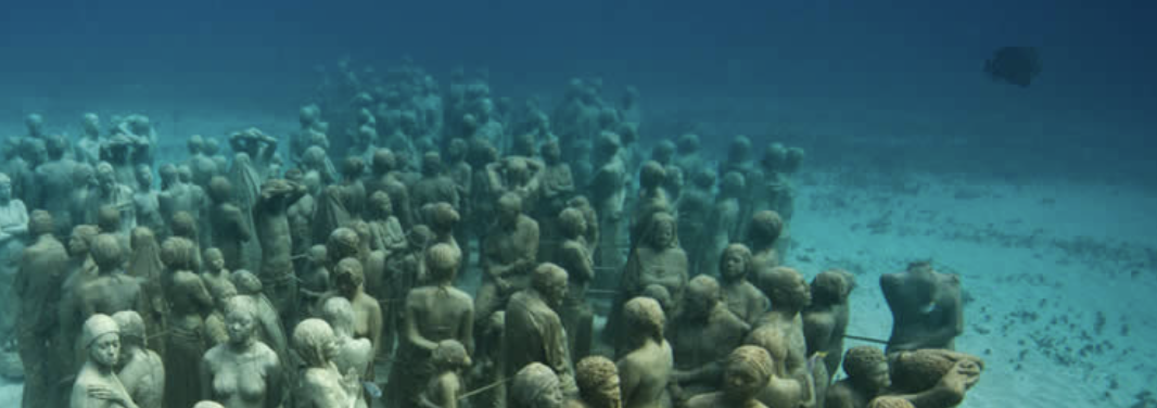 Buceador posando junto a la escultura de un auto Volkswagen Beetle cubierto de vida marina en el MUSA de Cancún.