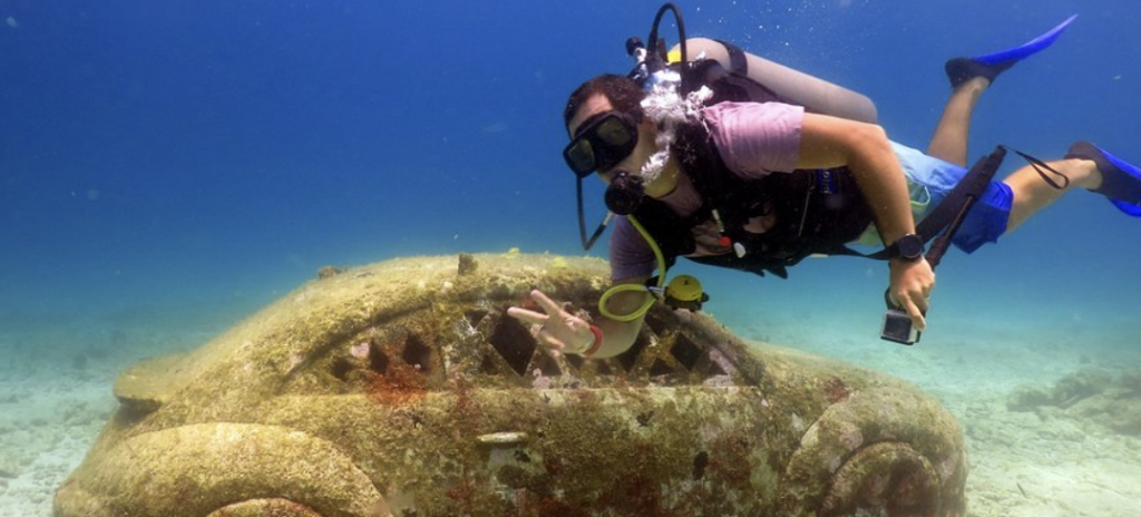 Scuba diver exploring a coral-covered Volkswagen Beetle