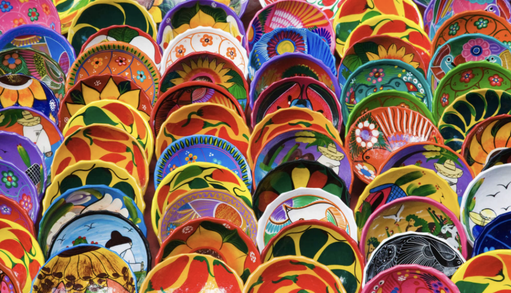 Primer plano de una gran colección de platos y cuencos de cerámica mexicana pintados a mano con colores vibrantes y diseños florales tradicionales.