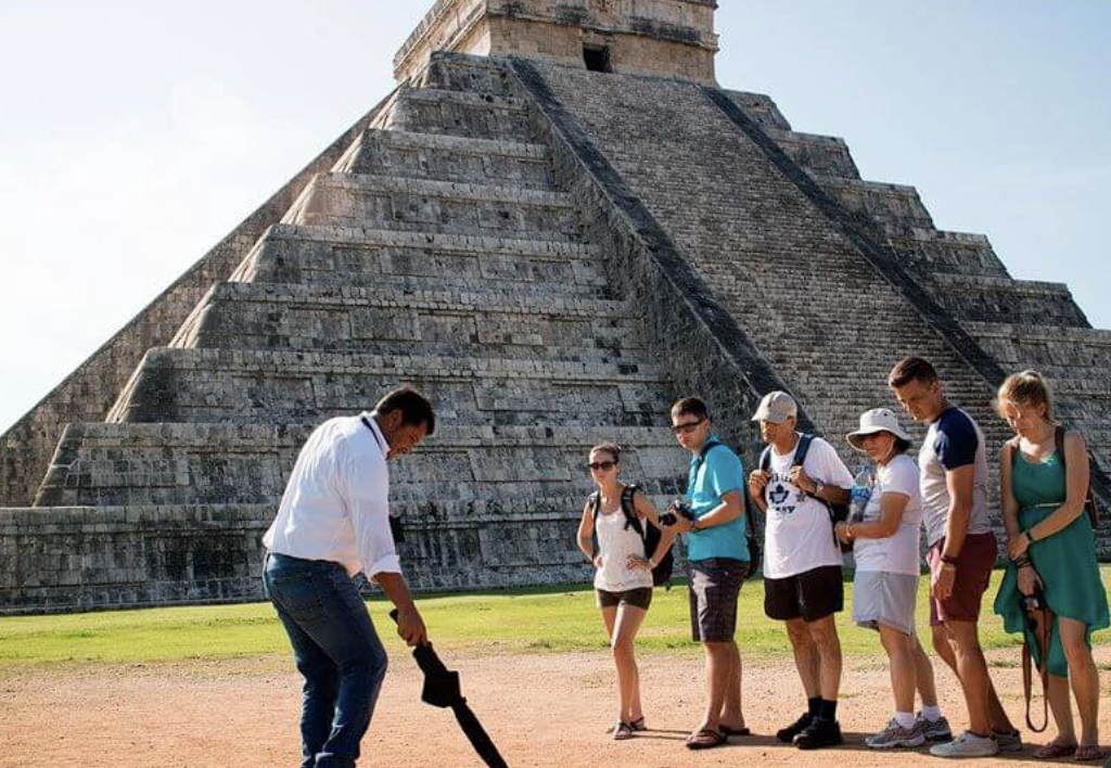 Guía turístico explicando la historia de la Pirámide de Kukulcán a un grupo de visitantes en Chichén Itzá.